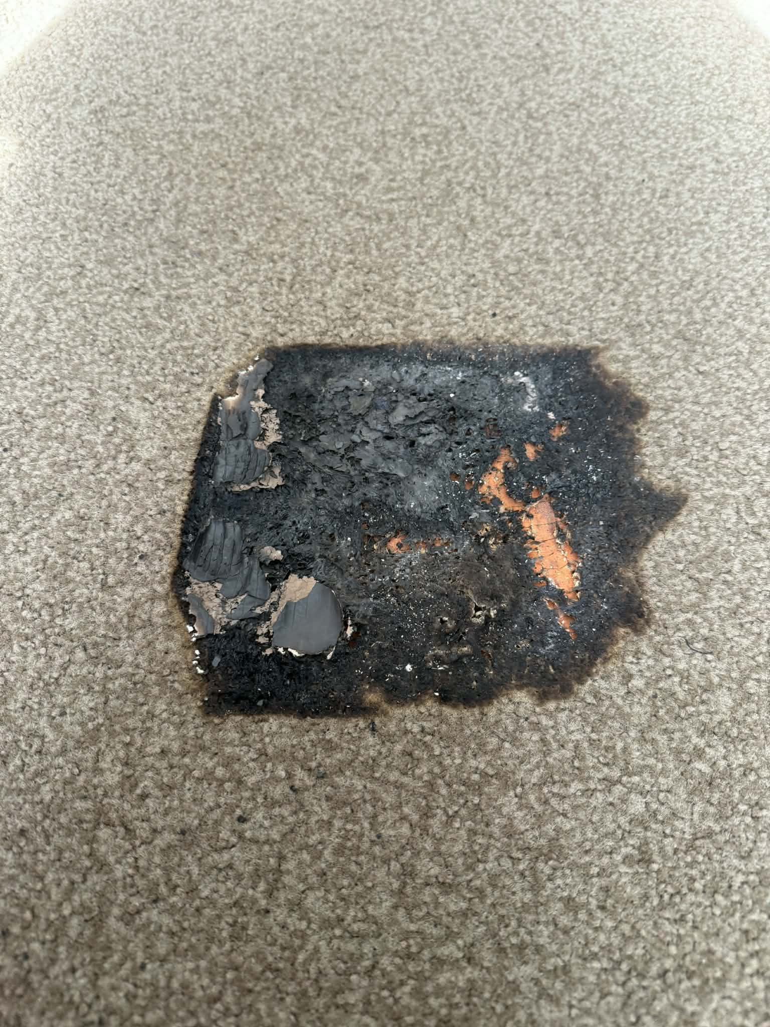 Beige carpet with a large melted burn mark in the centre before restoration