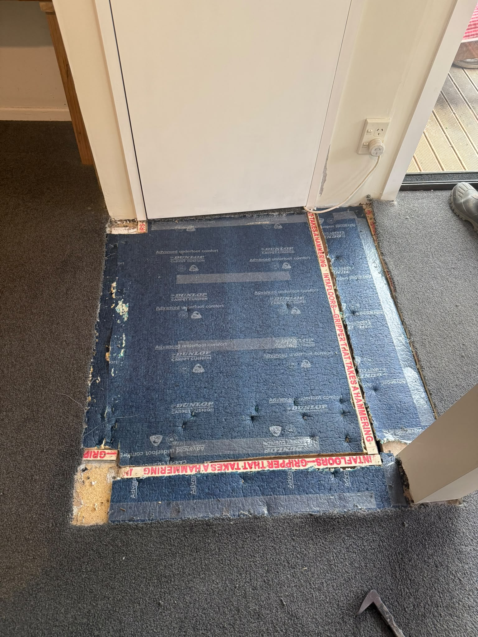Carpet lifted back at the deck doorway exposing the blue underlay and gripper strips