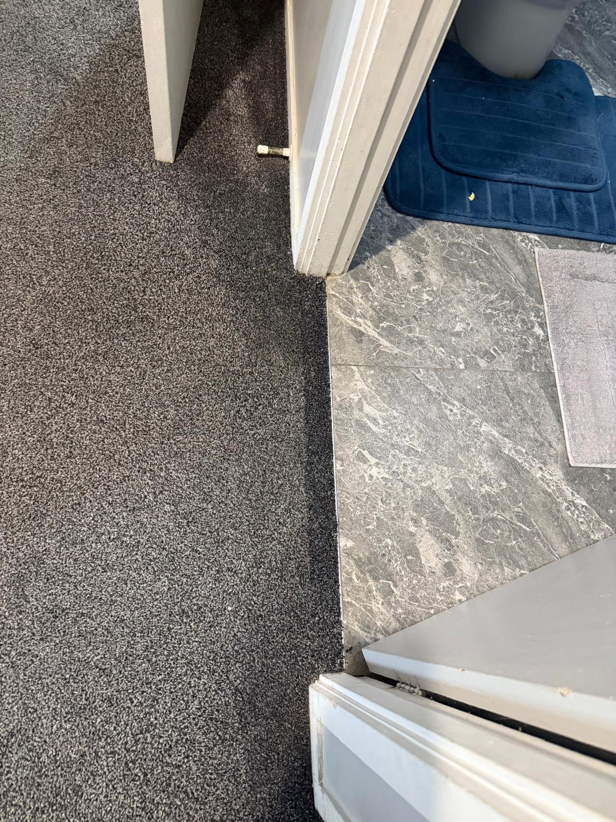 The same bathroom doorway after repair, with the charcoal carpet edge finished cleanly against the marble tile